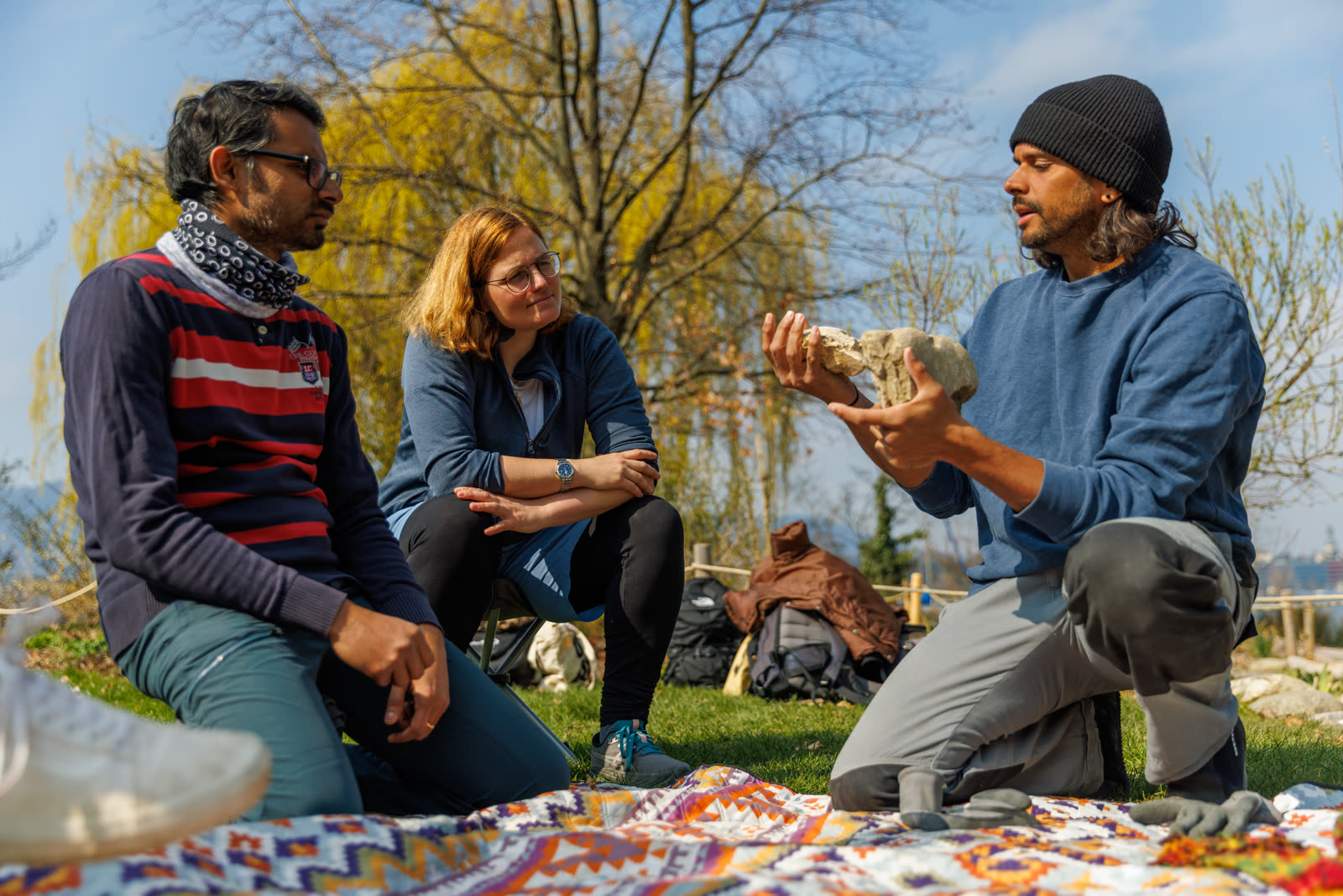 Greg explaining a stone's balance point to two workshop guests on a picnic blanket