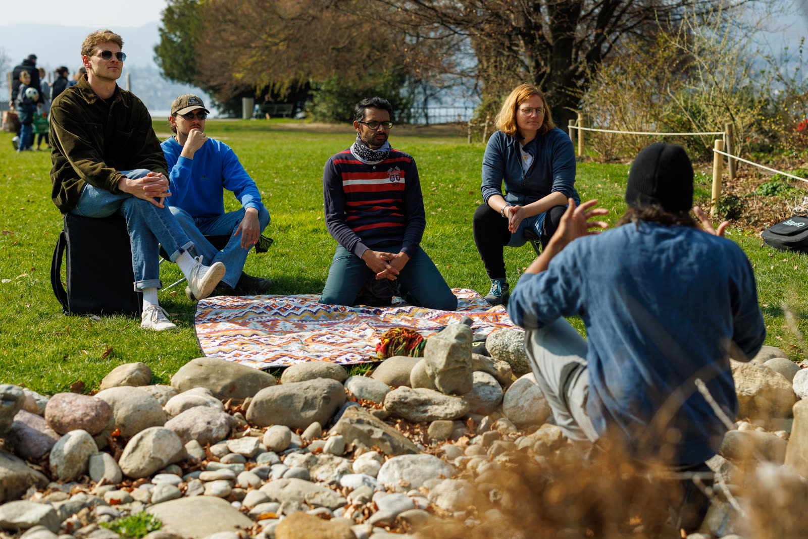 A workshop group sitting in the sun listening to Greg by the lakeside stone garden