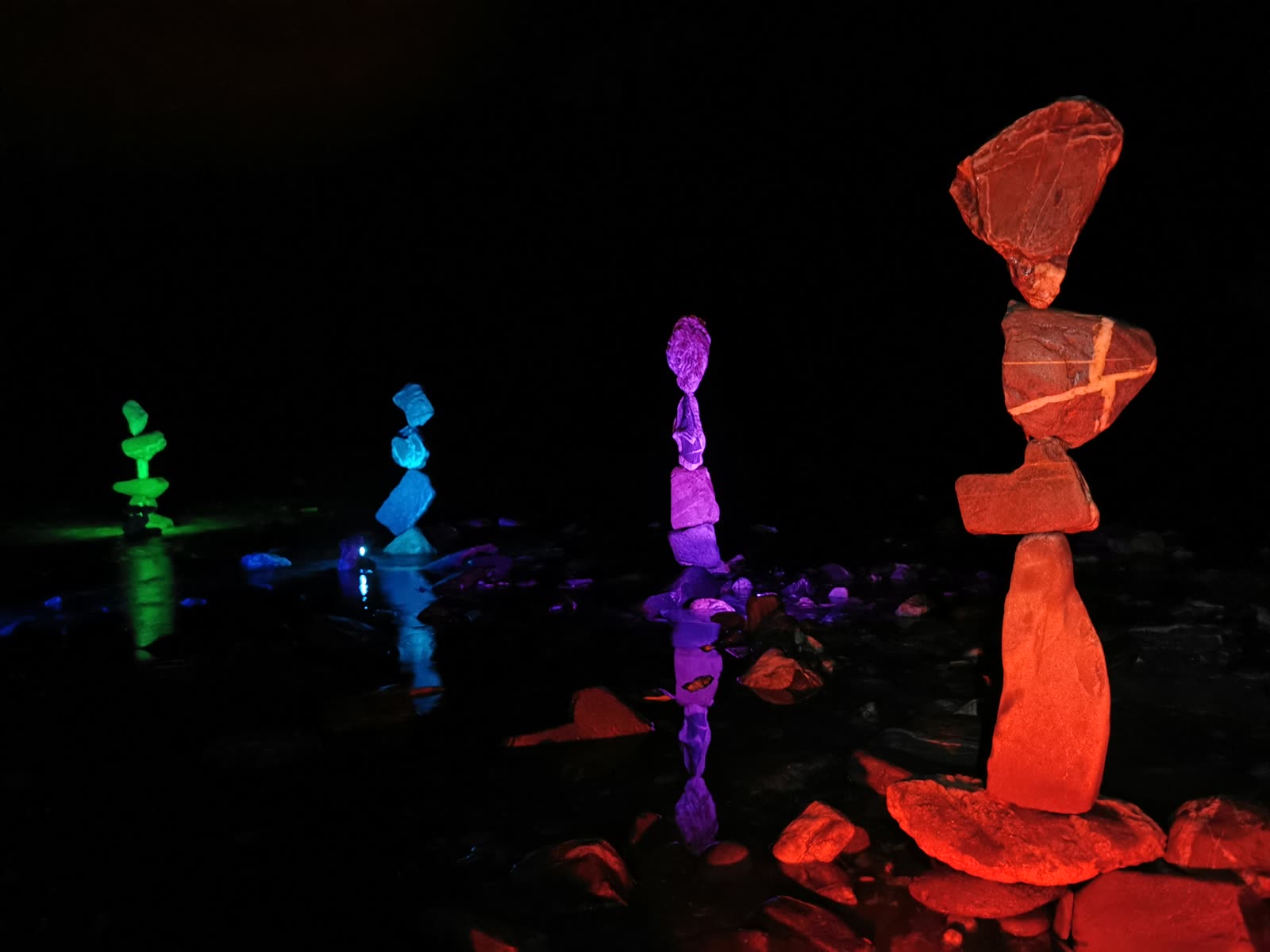Stone towers lit in green, blue, purple and red reflecting on the Rhine at night