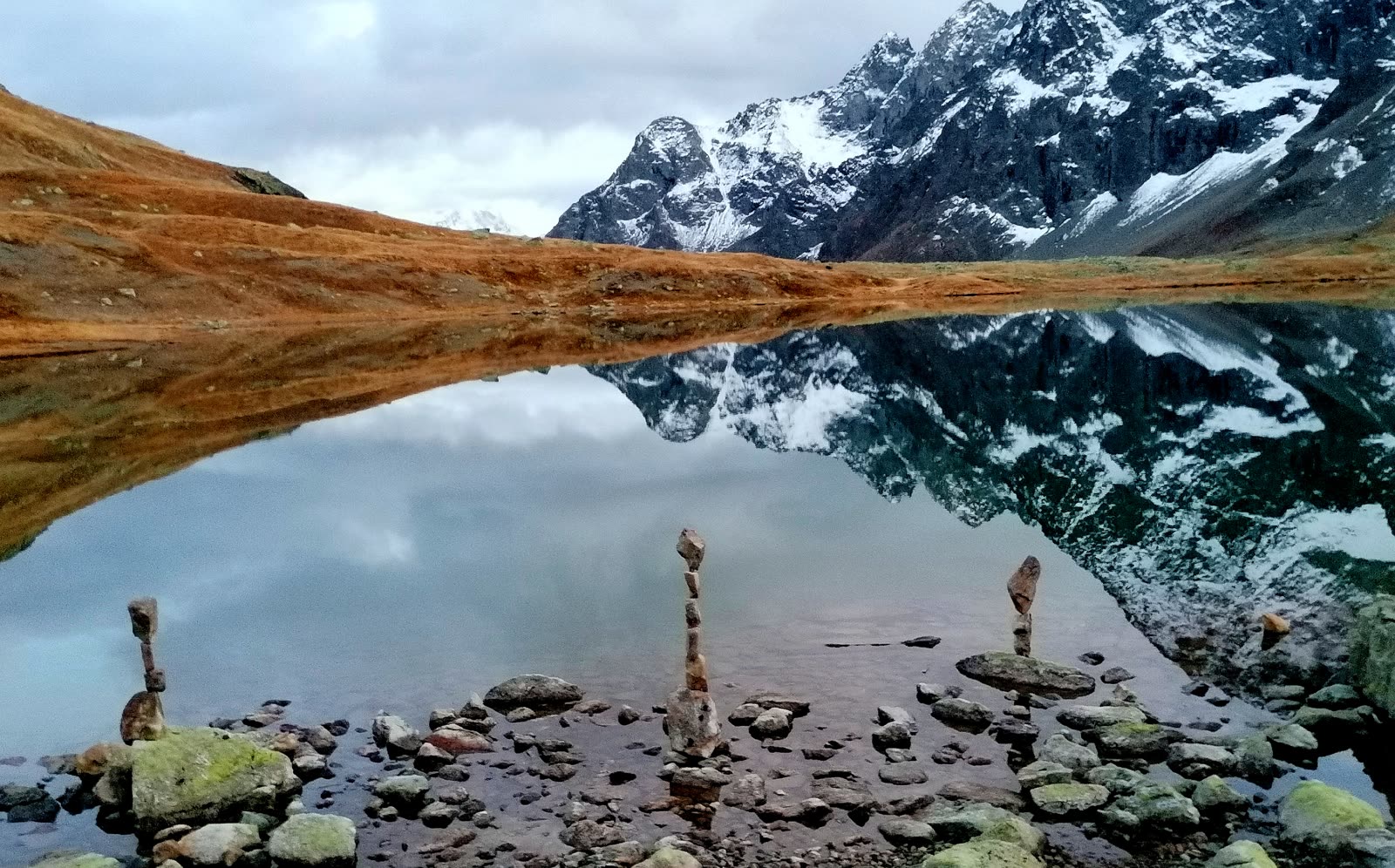 Balanced stones before a mirror-still alpine lake and snow peaks near St. Moritz